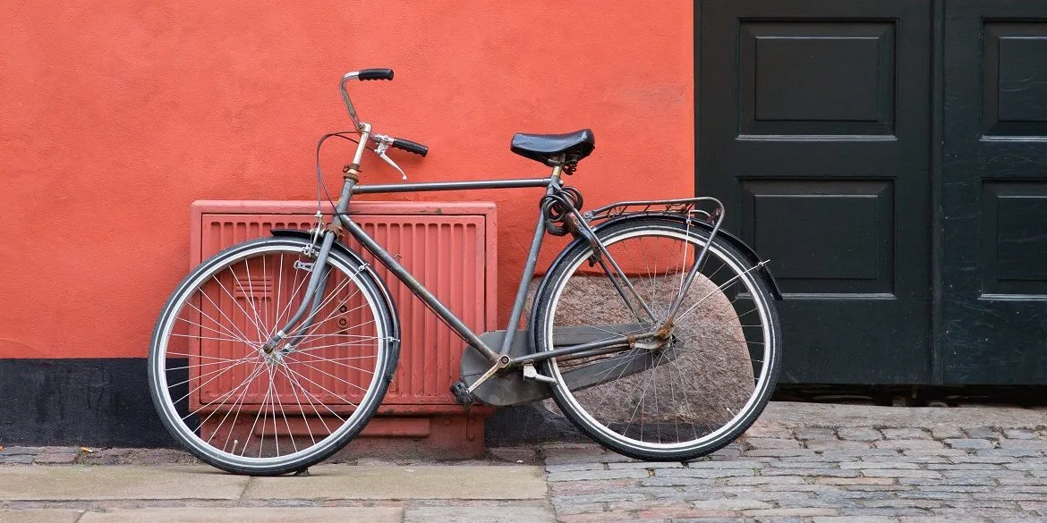 marten-bjork-Lpe9u9etwMU-unsplash small grey bike against a coral coloured wall