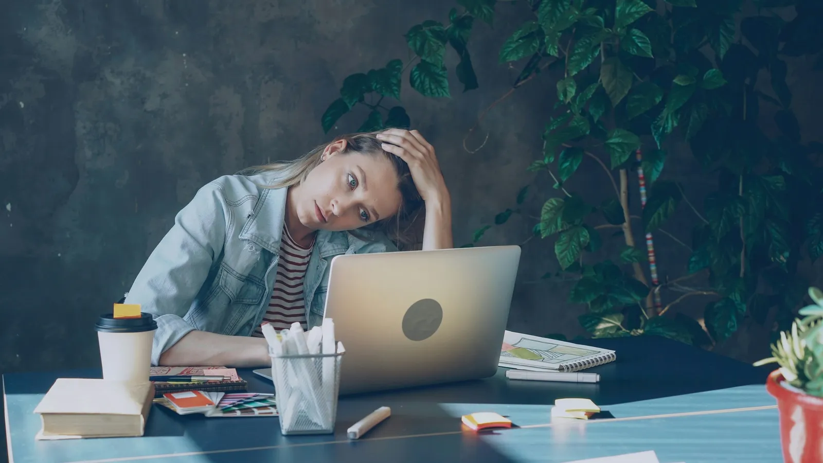 a woman in front of her laptop at a desk holds her head in her hand and looks worried signifying a lack of psychological safety