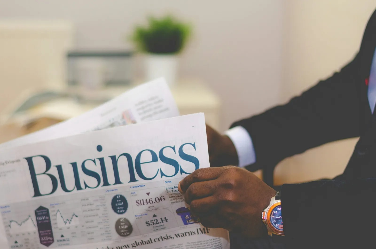 picture of a black man's hands holding a business newspaper. The man is wearing a dark suit and a white shirt. The newspaper signifies development of people management skills